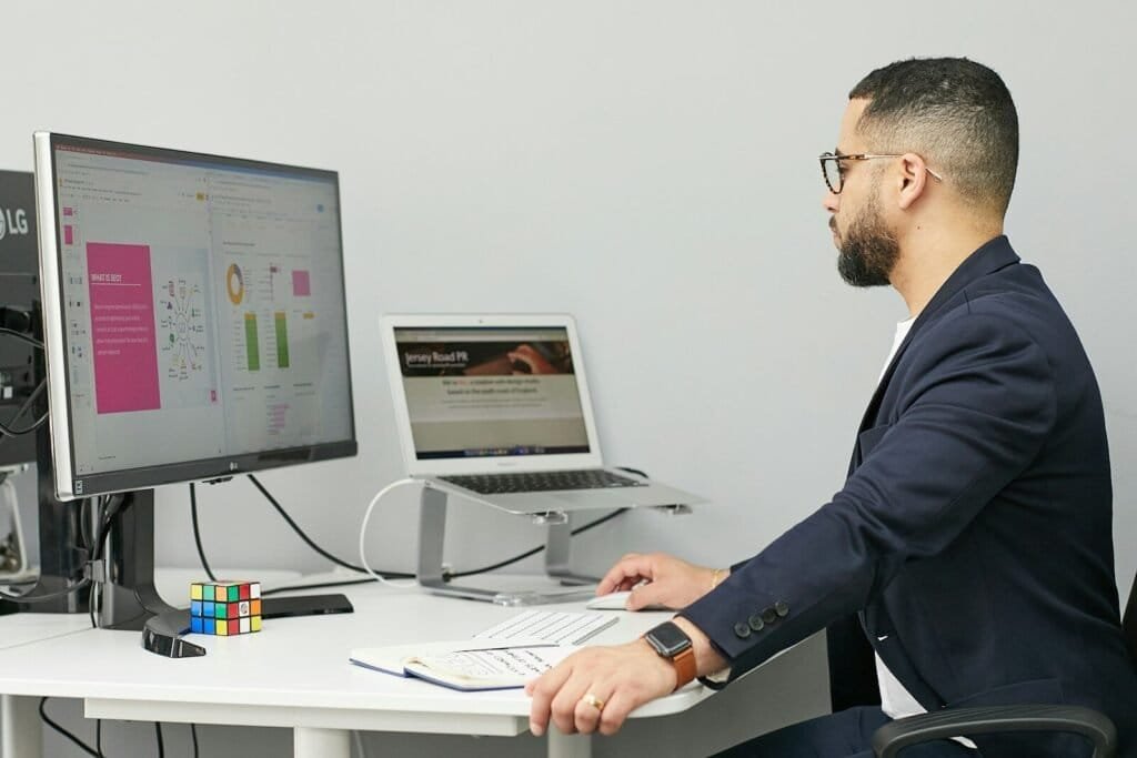 A Man Sitting At A Desk With A Laptop And A Computer