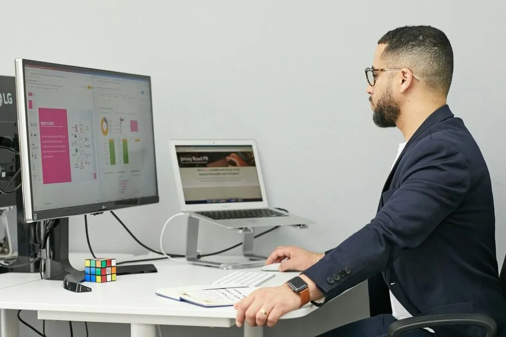 A Man Sitting At A Desk With A Laptop And A Computer