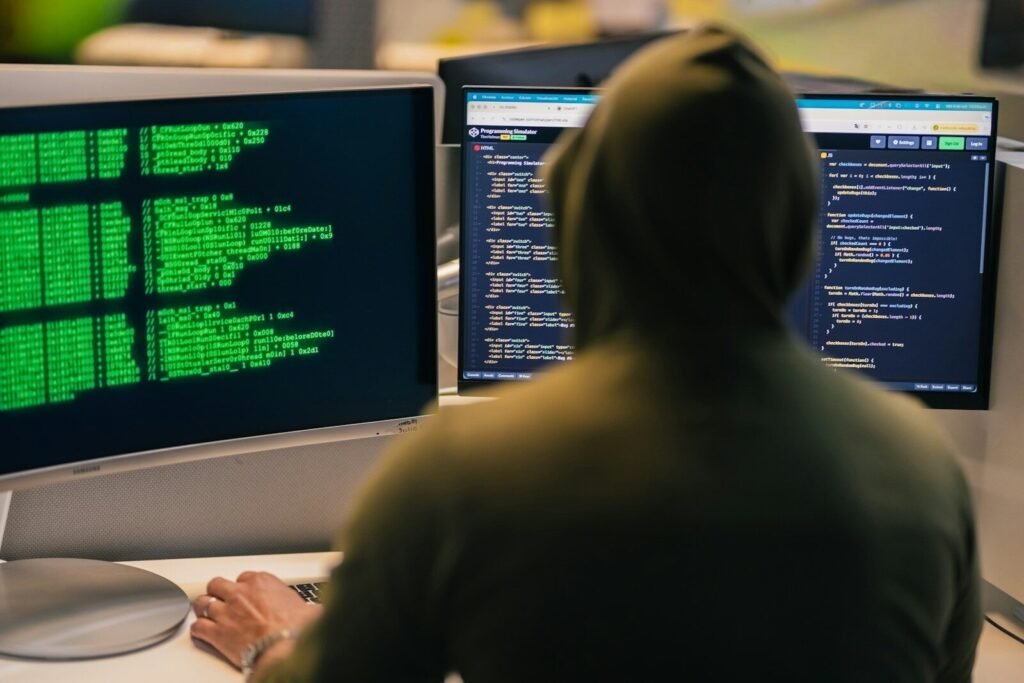 Hacker In Hoodie Working On Multiple Computer Screens